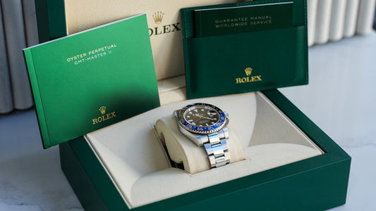 Close-up of a Rolex Oyster Perpetual GMT-Master II watch in its green box with warranty and manual papers.